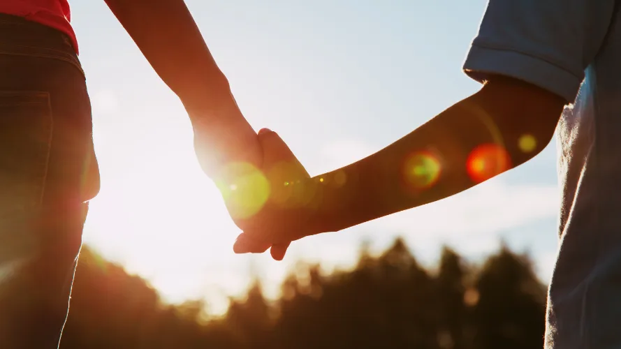 Parent and child holding hands in sunset.