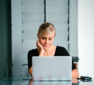 Woman sitting at table looking at laptop computer.